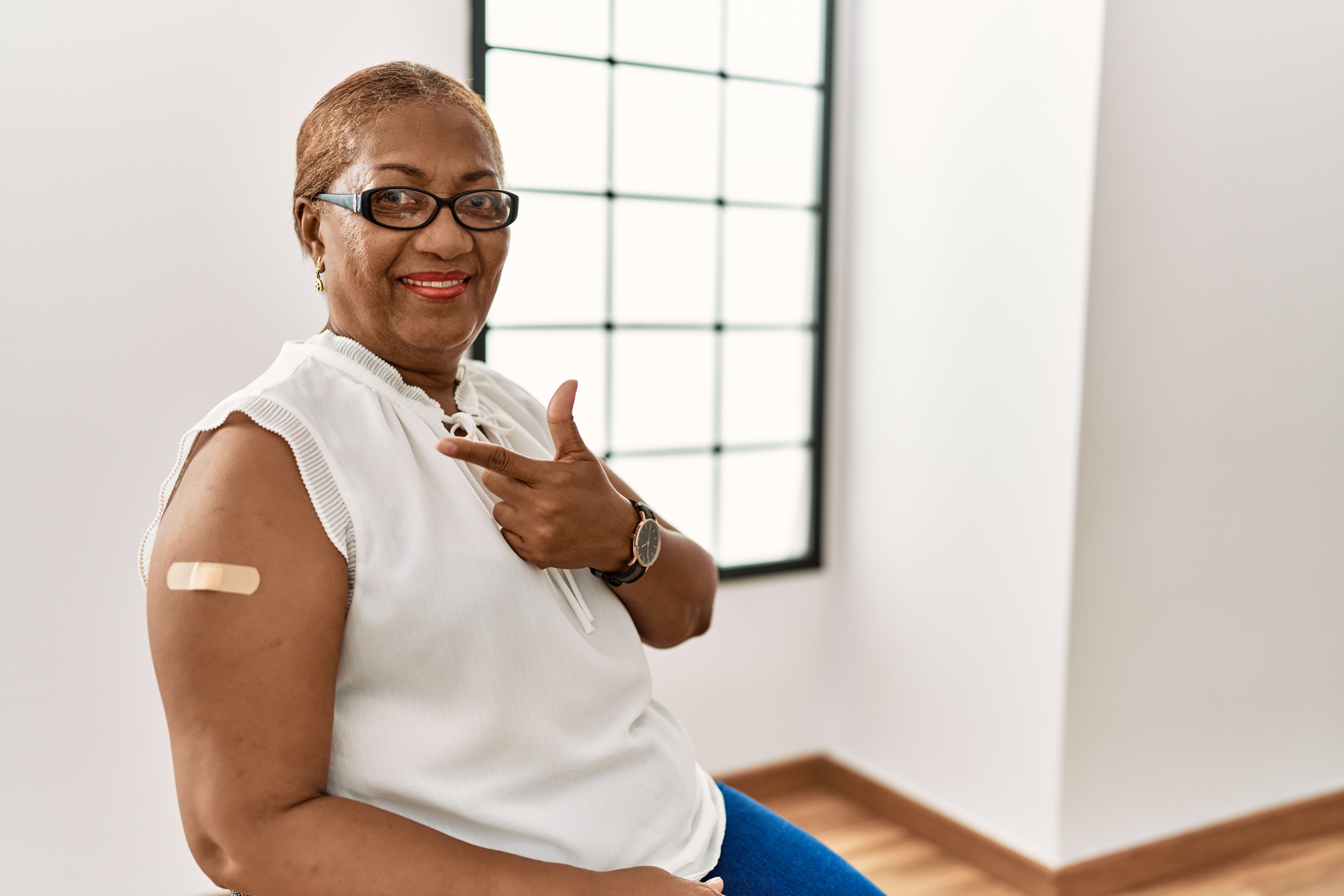 Mature hispanic woman getting vaccine showing arm with band aid cheerful with a smile on face pointing with hand and finger up to the side with happy and natural expression