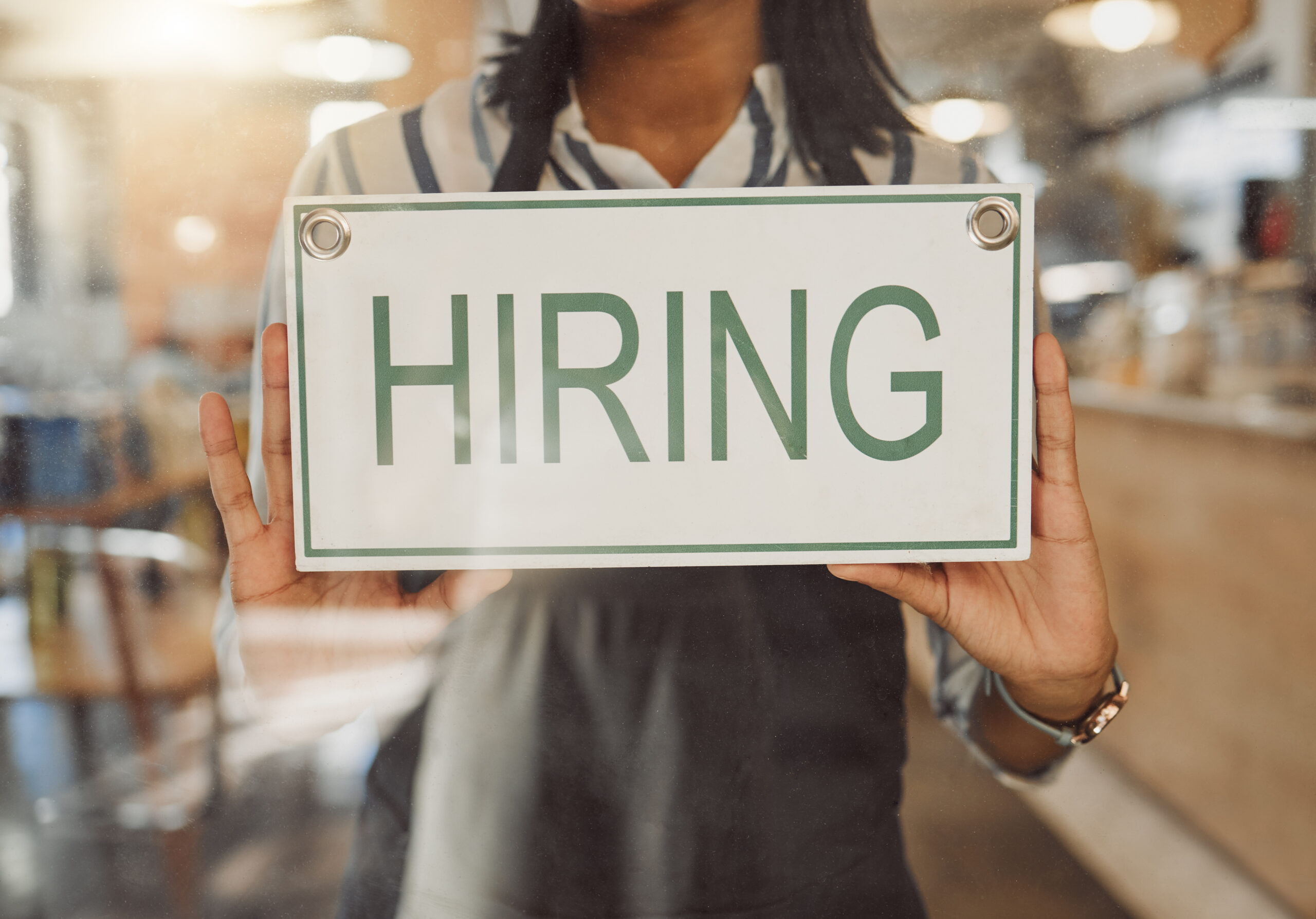 Hands of business owner holding hiring sign. Businesswoman hanging hiring sign in cafe entrance.